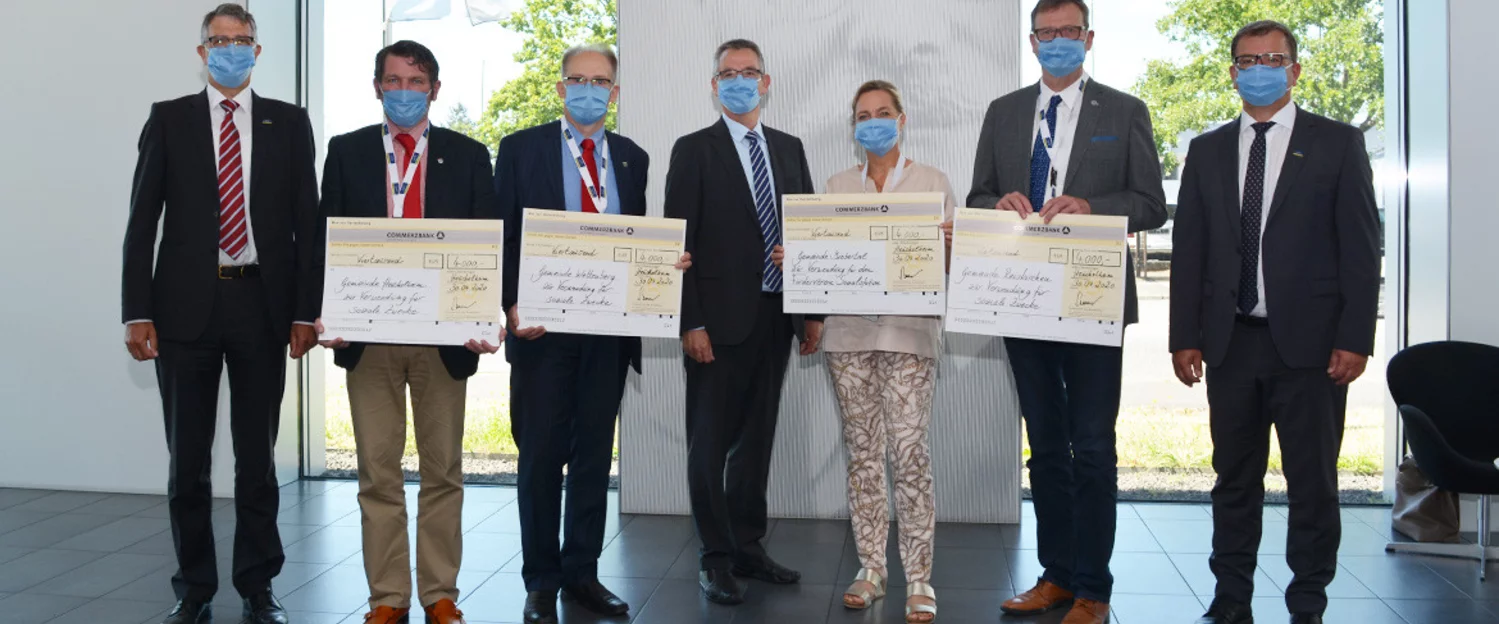 7 Personen stehen nebeneinander in einer Reihe und halten den Spendencheck