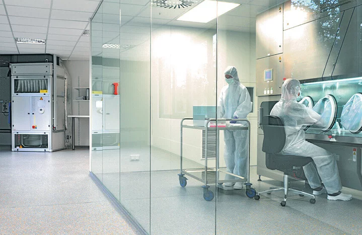 GMP‑compliant cleanroom for pharmacy compounding with isolator workstation and personnel in full cleanroom garments.